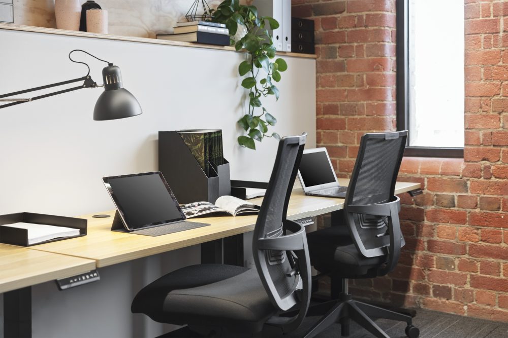 Modern office space with ergonomic task chairs and desk, decorated shelves and red brick wall