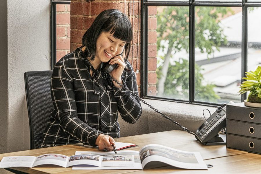 young professional woman making phone calls at a desk next to the window in a modern office space