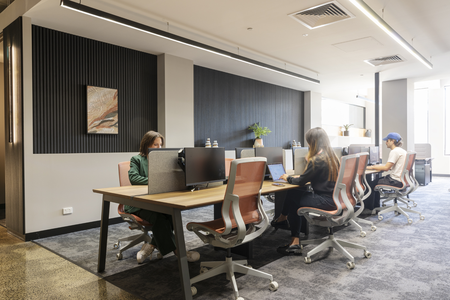 A coworking space with desks and monitors filled with natural light. multiple people working independently and collaboratively.