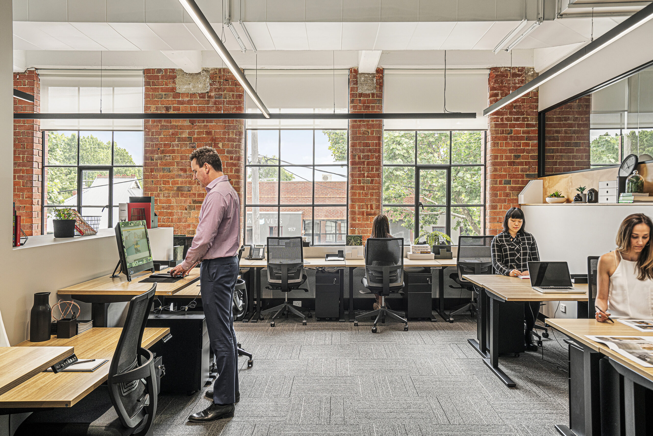 team working in a shared office space with large windows letting in natural light person working at a sit to stand desk in an office